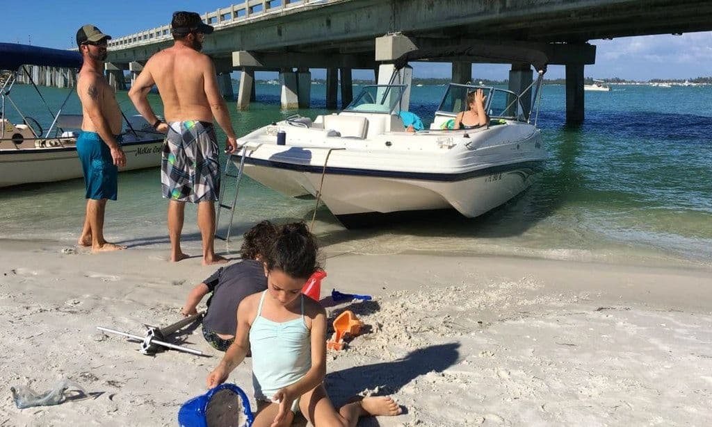 Family enjoying a beach day near a boat under a pier with sand and water activities.