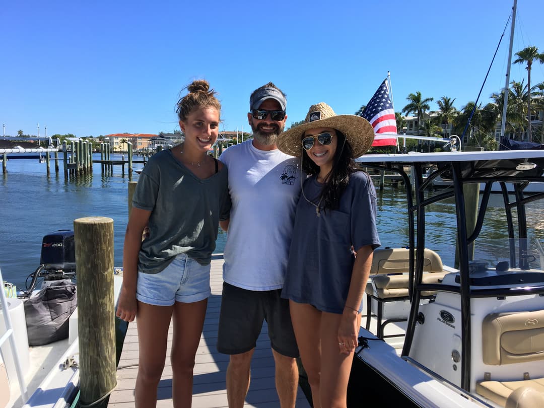 Group photo on a dock with a boat, featuring two women and a man, sunny day, American flag visible.
